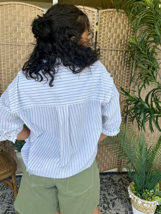 Light blue pinstriped button-up shirt with puffed sleeves worn with sage green shorts.
