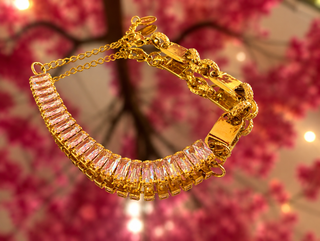 Gold-plated Quinn bracelet with rectangular crystals and chain links against pink floral background.
