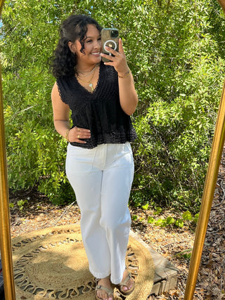 Black textured V-neck sleeveless top with lace trim paired with white pants.
