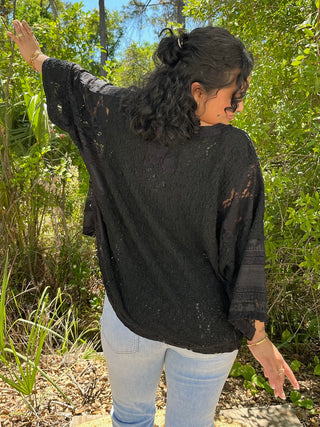 Black lace beachy top with handkerchief hem and sheer sleeves styled with light wash jeans.
