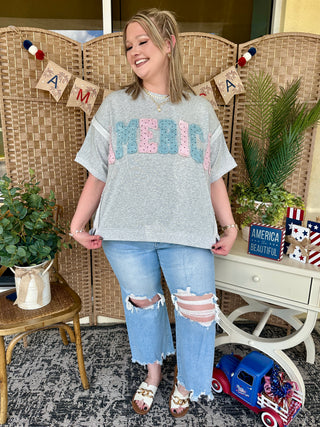 Gray t-shirt with blue and pink polka dot Americana graphic, styled with distressed blue jeans.

