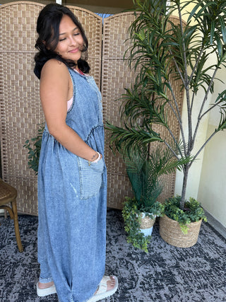 Blue denim sleeveless jumpsuit with large front pockets and relaxed oversized fit.

