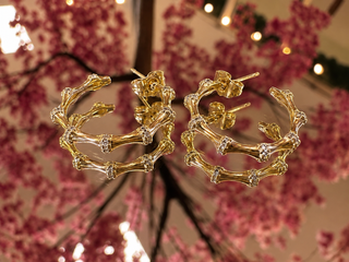 Gold bamboo hoop earrings with textured detailing displayed against pink floral background.
