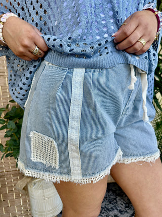 Light blue striped denim shorts with distressed holes and lace trim detailing.
