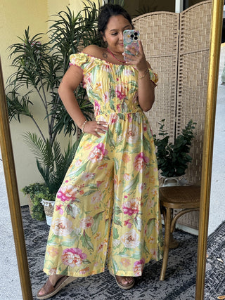 Yellow floral off-shoulder jumpsuit with pink and red flowers, short ruffled sleeves, and wide-leg pants.
