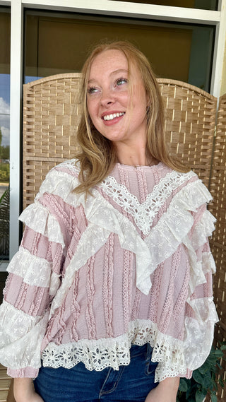 Pink and cream ruffled blouse with lace trim and eyelet details, worn with dark denim.
