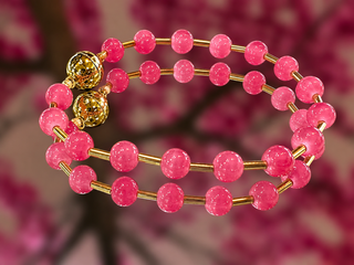 Pink glass beaded bracelet with gold-tone magnetic accents on blurred floral background.
