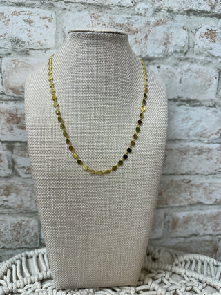 Gold disc bead necklace with alternating metallic beads on cream linen display bust.
