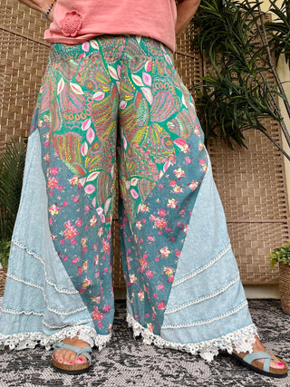 Teal wide-leg pants with colorful floral and paisley print, light denim patchwork, and lace trim hem.
