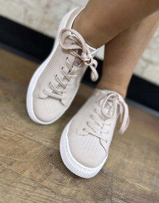 Dusty pink knit mesh lace-up sneaker with white sole on wooden floor.
