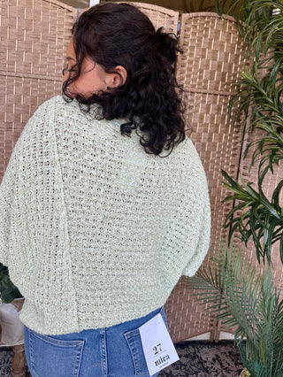 Cream open-weave asymmetrical sweater top worn with blue jeans, back view.
