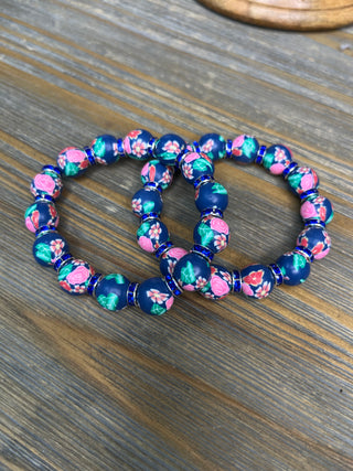 Navy and pink floral clay bead stretch bracelets with turquoise accents on wooden surface.
