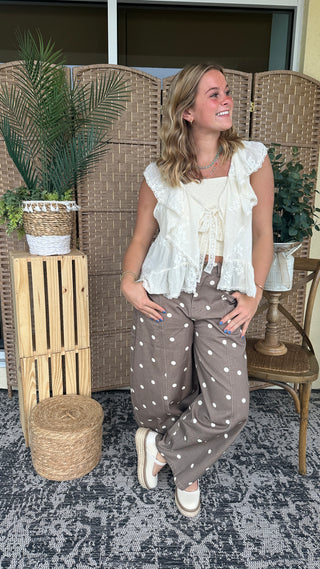 White lace ruffle sleeveless vest top with tie-front detail paired with taupe polka dot pants.
