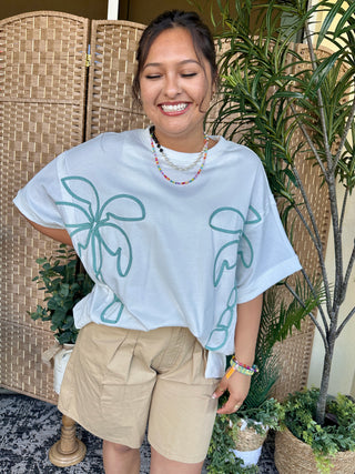 White oversized tee with teal palm tree graphic print and short sleeves.
