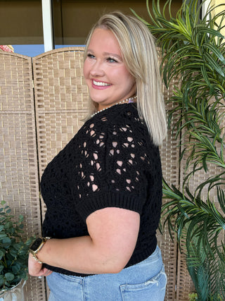 Black open weave cropped sweater with short sleeves and cutout detail.
