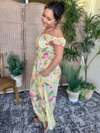 Yellow floral off-shoulder jumpsuit with pink and green flowers, ruched detailing, and wide legs.

