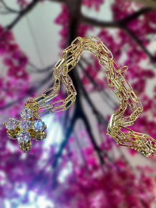 Gold chain necklace with sparkling rhinestone cross pendant on floral background.
