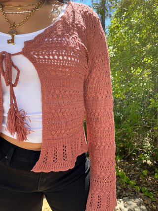 Terracotta crochet cardigan with openwork pattern and tassel tie-front detail over white top.
