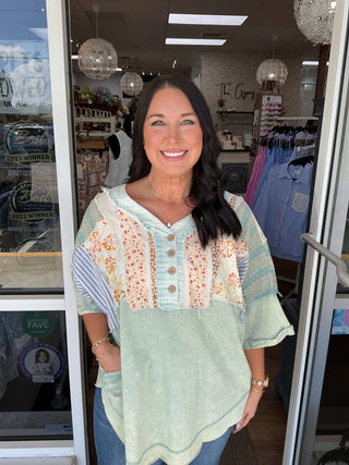 Sage Mineral Washed Patchwork Henley Top with button detailing, long sleeves, and a relaxed fit on a hanger.