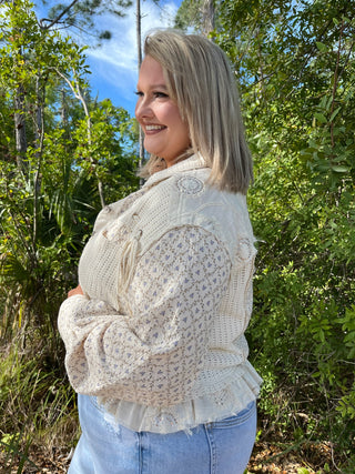 Cream quilted jacket with delicate floral print and lace details over blue jeans.
