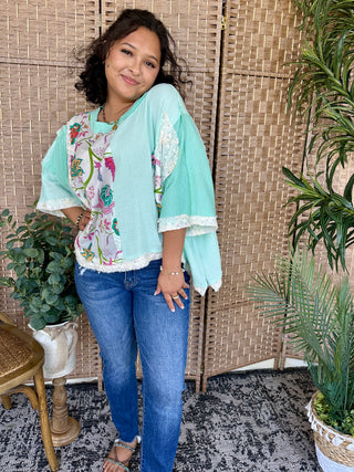 Mint oversized top with floral and lace colorblock design, paired with blue jeans.
