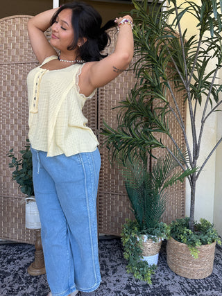 Cream waffle-knit sleeveless tank top with lace trim and button details, paired with blue jeans.
