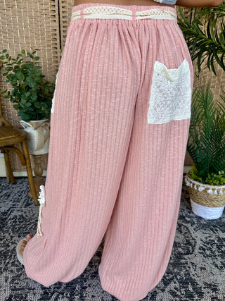 Pink ribbed joggers with cream lace pocket and waistband trim, shown from back view.
