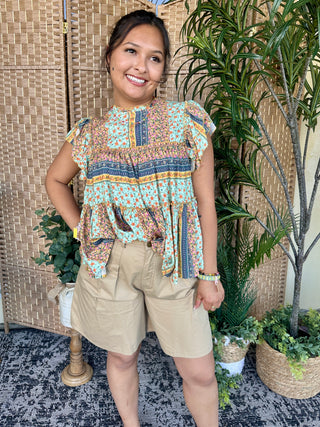 Turquoise floral print blouse with ruffled short sleeves and navy stripe trim detail.
