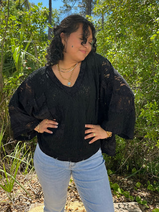 Black lace beachy top with handkerchief hem and flutter sleeves paired with light blue jeans.
