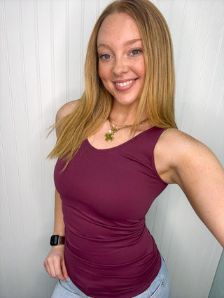 Plum sleeveless tank top with ruched sides on model wearing light jeans.
