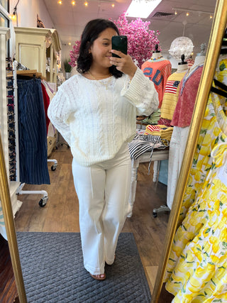 Ivory cable knit sweater with long sleeves styled with white pants in a dressing room mirror.
