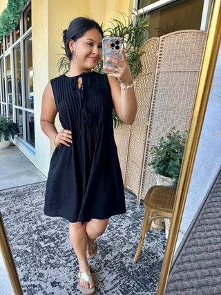 Black sleeveless pintuck dress with keyhole neckline detail on model.
