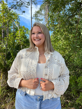 Ivory floral lace jacket with button front and textured details over white tank top.
