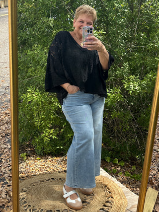 Black lace handkerchief top with textured fabric and flutter sleeves paired with light blue jeans.
