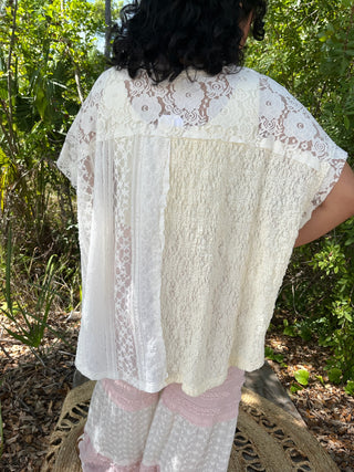 Ivory lace short-sleeve top with mixed lace panels and handkerchief hem, worn over patterned dress.
