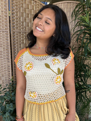 Cream open crochet top with orange trim and embroidered lemon slice and leaf details.

