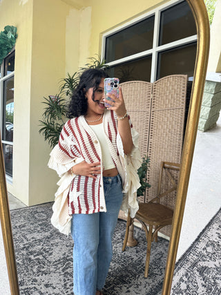 Red and white striped knit cardigan with ruffled sleeves over cream camisole, worn with blue jeans.
