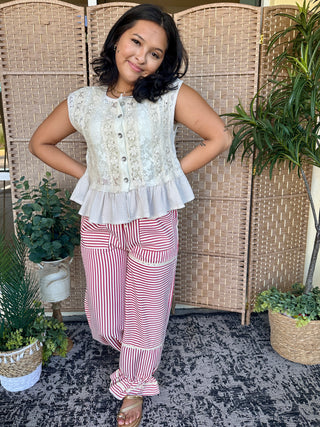 Cream lace sleeveless top with button front and ruffle tier hem paired with red and white striped pants.

