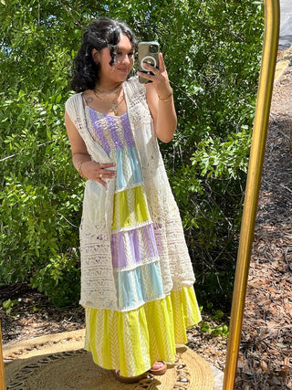Cream crochet sleeveless vest worn over colorblock tank top in purple, blue, and yellow tones.

