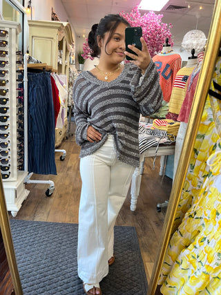 Black and gray striped v-neck sweater worn with white pants in boutique dressing room.
