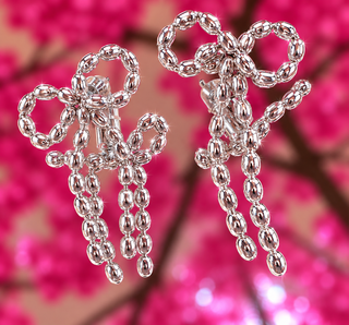 Silver beaded bow drop earrings with cascading bead strands against pink floral background.
