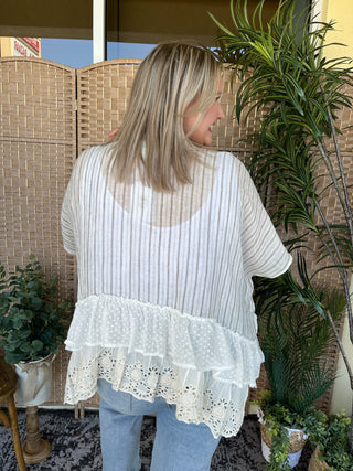 White striped kimono top with ruffled lace hem, worn with light blue jeans.
