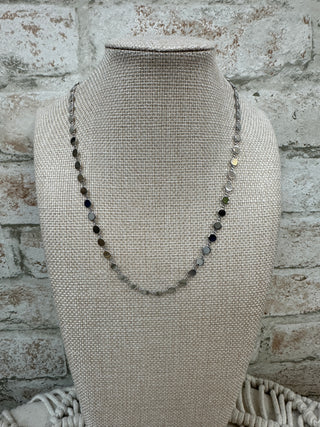 Silver beaded necklace with black onyx disc accents on linen display bust.
