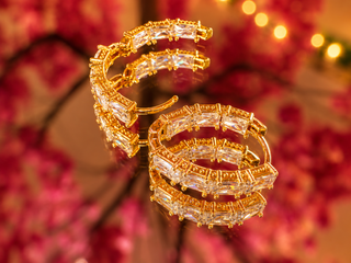 Gold ice crystal huggie hoop earrings with baguette-cut cubic zirconia detailing, displayed against pink floral background.
