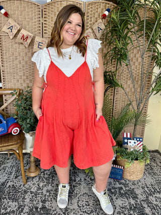 Red denim romper with white eyelet ruffle sleeves and adjustable straps.
