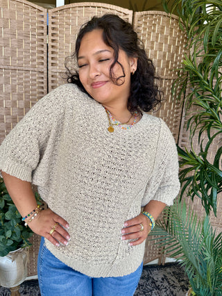 Taupe knit sweater with textured asymmetrical design and short sleeves.
