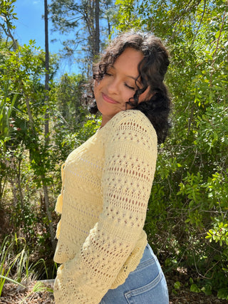 Cream knit cardigan with openwork pattern and fringe trim over blue jeans.
