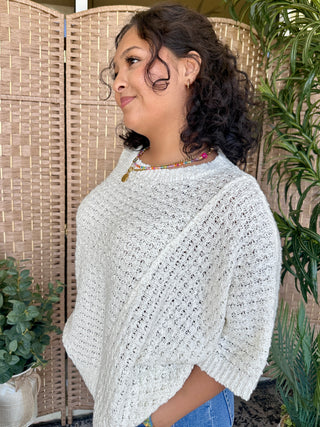 Off-white asymmetrical knit sweater with open-weave texture and crew neckline.
