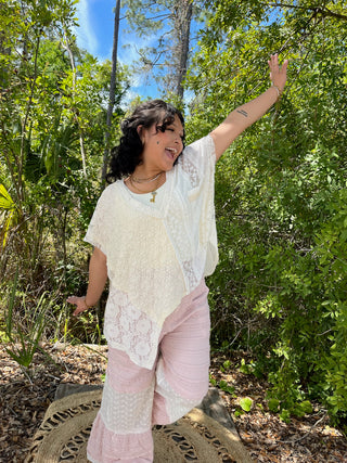 Ivory lace handkerchief top with short sleeves and asymmetrical hem, worn with pink pants.

