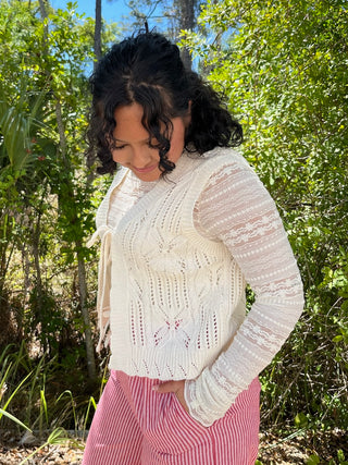 Ivory cable knit sweater with tie-front detail and textured sleeves worn with pink striped pants.
